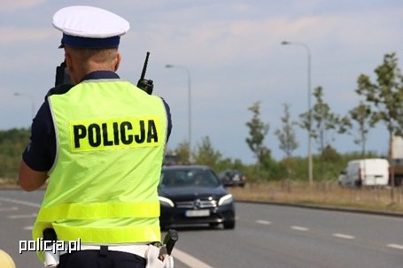 policjant ruchu drogowego stoi przy drodze, w tle jadący samochód