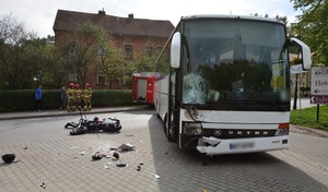 Na  pierwszym planie uszkodzony autobus i leżący obok zniszczony motocykl, w tle strażacy.
