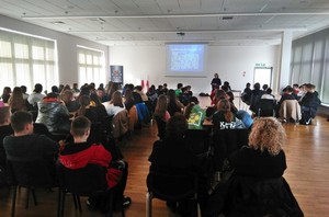 Na pierwszym planie młodzież uczestnicząca w spotkaniu dotyczącym zagadnień bezpieczeństwa, organizowanym na terenie auli konferencyjnej krośnieńskiej komendy. W tle policjantka w trakcie wykładu, obok ekran z wyświetlaną prezentacją multimedialną