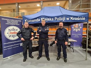 Policjanci w umundurowaniu służbowym przy stoisku informacyjnym w czasie „Dnia otwartego” uczelni w Sanoku. W tle namiot profilaktyczny oraz rolap Komendy Miejskiej Policji w Krośnie