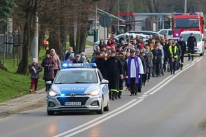 Policyjny radiowóz na przedzie kolumny pielgrzymów w czasie drogi krzyżowej ulicami miasta. W tle uczestnicy procesji