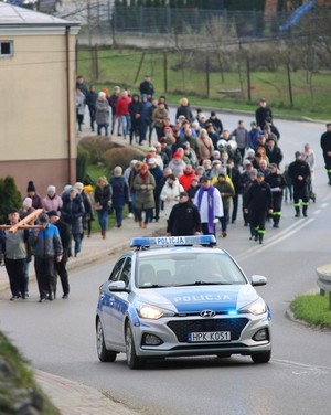 Policyjny radiowóz na przedzie kolumny pielgrzymów w czasie drogi krzyżowej ulicami miasta. W tle uczestnicy procesji