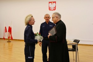 Policjantka wręcza kwiaty księdzu. W tle Komendant Miejski Policji w Krośnie