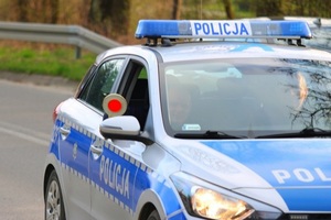 Policjanci w oznakowanym radiowozie. Jeden z nich przez otwarte okno daje sygnał do zatrzymania pojazdu