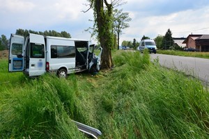 Znajdujący się poza drogą bus. Przednia część pojazdu zniszczona po zderzeniu z drzewem. Na ulicy policyjny radiowóz