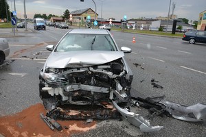 Uszkodzenia przedniej części toyoty, w tle policyjny radiowóz i skrzyżowanie, na którym doszło do wypadku