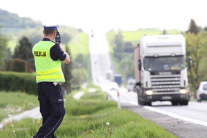 Policjant kontrolujący prędkość na drodze. Na dalszym planie nadjeżdżające pojazdy