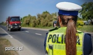 Na pierwszym planie znajduje się policjantka ruchu drogowego wykonująca pomiar prędkości