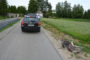 Stojący na jezdni samochód, tuż za nim leżący na poboczu uszkodzony rower