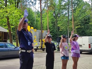 Policjant prezentujący pokaz ręcznego kierowania ruchem obok uczestniczące w spotkaniu dzieci