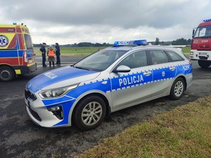 policyjny radiowóz na płycie lotniska, obok strażackie wozy bojowe