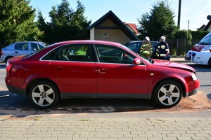 Uszkodzenia pokolizyjne przedniej części audi, w tle pracujący na miejscu strażacy