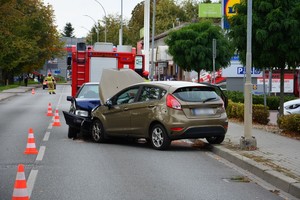 Uszkodzenia powypadkowe pojazdów, na dalszym planie samochód strażacki. Obok ustawione na jezdni pachołki drogowe