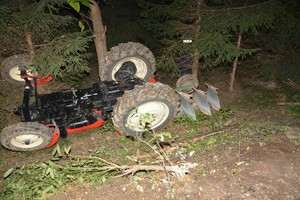 Przewrócony ciągnik rolniczy w zagłębieniu terenu przy drodze gruntowej