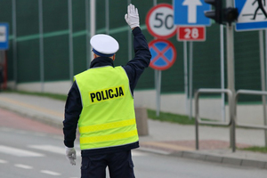 Policjant regulujący ruchem na skrzyżowaniu z podniesioną do góry prawą ręką