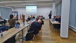 Uczestnicy podczas debaty w auli konferencyjnej. W tle prelegent i wyświetlana prezentacja multimedialna