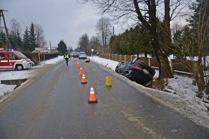 Przewrócone na dach audi w przydrożnym rowie. W tle pojazdy służb ratowniczych