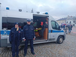 Funkcjonariusze na tle radiowozu podczas zabezpieczenia 32 finału Wielkiej Orkiestry Świątecznej Pomocy