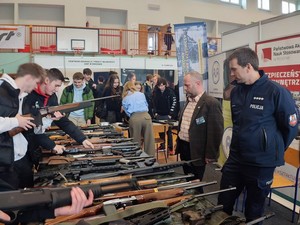 policjant i instruktor prezentują broń młodzieży podczas targów pracy