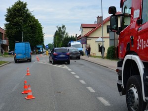 miejsce kolizji drogowej. W tle uszkodzone pojazdy oraz radiowóz. Na pierwszym planie pojazd strażacki