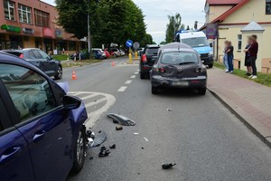 Miejsce kolizji drogowej. W tle uszkodzone pojazdy oraz radiowóz.