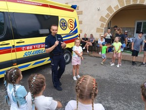 policjant na tle karetki pogotowia podczas rozmowy z dziećmi uczestniczącymi w pikniku rodzinnym