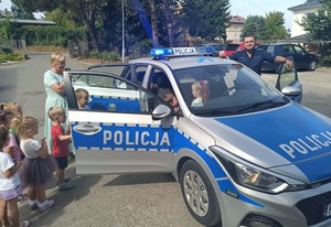 przedszkolaki we wnętrzu radiowozu w ramach organizowanego spotkania profilaktycznego. Obok radiowozu policjant prowadzący spotkanie