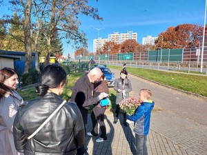 osoby kwestujące w rejonie cmentarza, w tle policjant  podczas działań związanych z obchodami Wszystkich Świętych