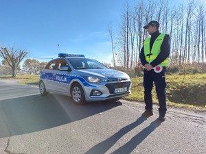 policjant  stojący przy radiowozie podczas działań związanych z obchodami Wszystkich Świętych