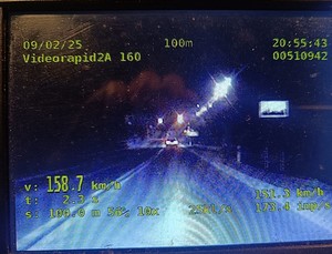 zdjęcie ekranu policyjnego videorejestratora z nagrania rozpędzonego do prędkości 158 km/h pojazdu wraz z parametrami prowadzonego pomiaru. Nocna sceneria, na zdjęciu widoczna tylna część samochodu sprawcy wykroczenia drogowego