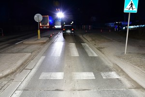Miejsce zdarzenia drogowego. Na pierwszym planie przejście dla pieszych, w tle pojazd uczestniczący w potrąceniu kobiety oraz policyjny radiowóz