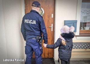 Policjant trzymający za rękę dziecko stojąc przy drzwiach mieszkania