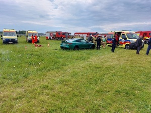 służby ratownicze na miejscu zdarzenia. Na trawie stojący samochód biorący udział w zdarzeniu