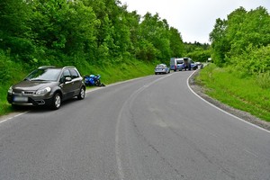 Miejsce wypadku drogowego. Na pierwszym planie samochód osobowy i znajdujący się za nim motocykl, w policyjne radiowozy