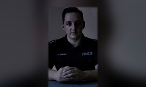 policjant w umundurowaniu służbowym na tle pokoju w szarej tonacji