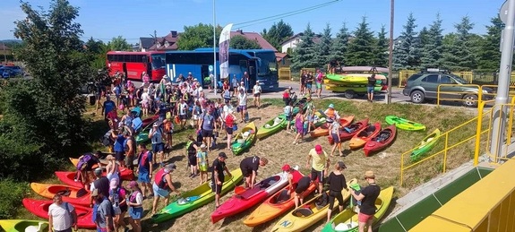 uczestnicy spływu kajakowego wraz ze sprzętem na brzegu rzeki przed startem