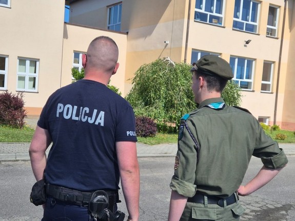 policjant i stojący obok niego harcerz podczas kontroli miejsca wakacyjnego wypoczynku