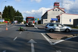 uszkodzenia powypadkowe pojazdów uczestniczących w wypadku. Leżący na jezdni motocykl, w tle pojazd strażacki