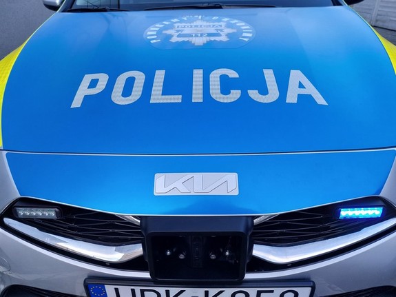 napis policja na niebieskim tle pokrywy silnika radiowozu oraz niebieskie sygnały świetlne przedniej części pojazdu