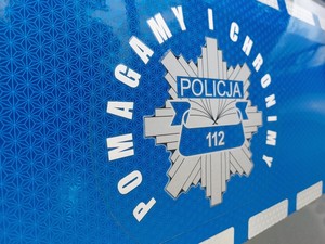hasło pomagamy i chronimy oraz grafika policyjnej gwiazdy na niebieskim tle pasa bocznego drzwi radiowozu