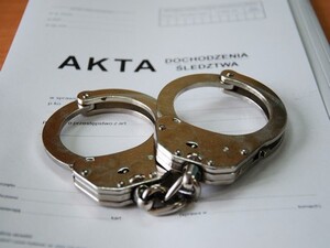Zdjęcie kajdanek oraz białek teczki z napisem "AKTA"
